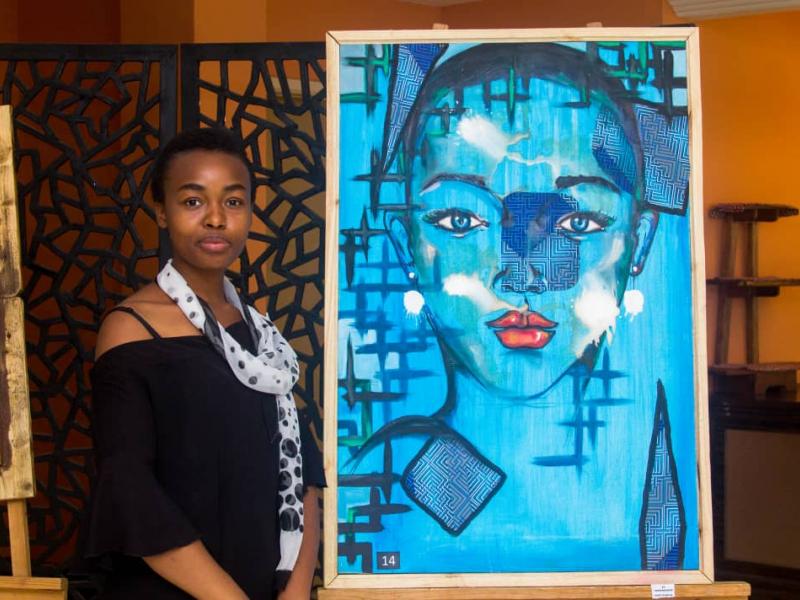 Légende : Mélissa Mujinga pose avec une des oeuvres d'arts.
