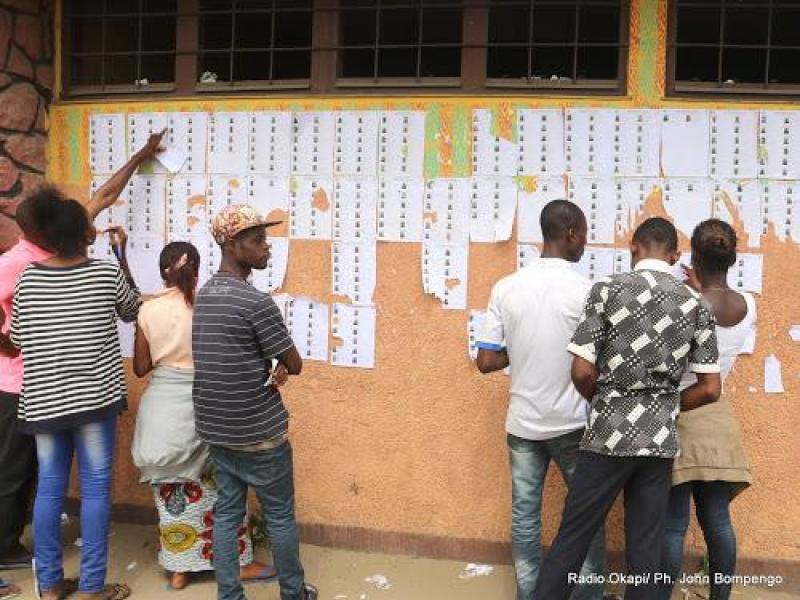 Quelques électeurs de Kinshasa vérifient leurs noms sur la liste devant les bureaux de vote