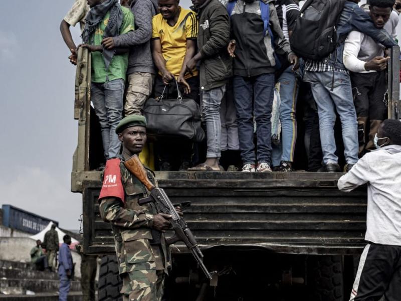 Un combattant du M23 monte la garde pendant que des personnes montent à bord d’un camion lors du recrutement de civils, de policiers, et d’anciens soldats de l’armée congolaise à Goma