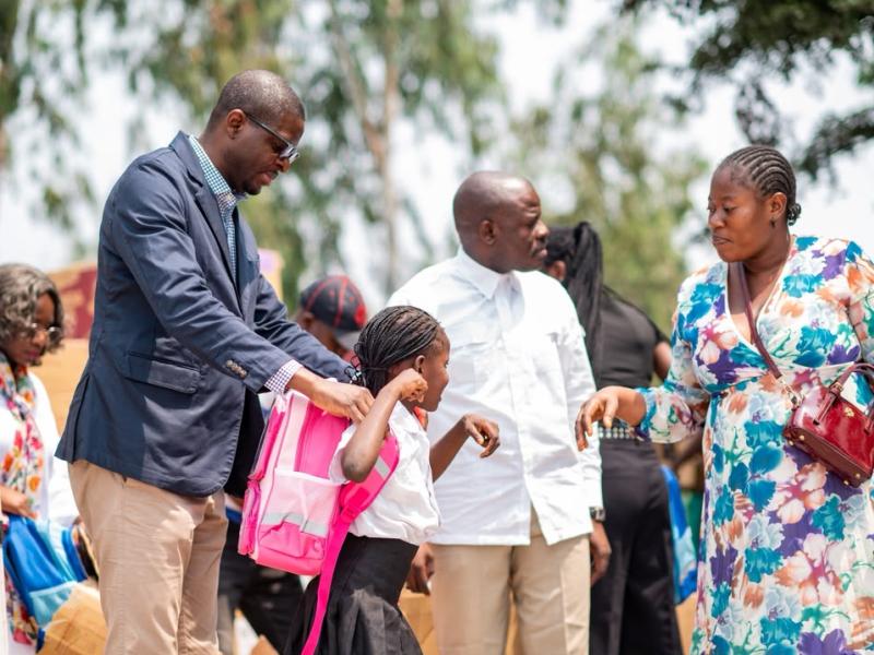 Le député national Éric Tshikuma, élu de la circonscription électorale de la FUNA, aide une écolière à enfiler son cartable lors de la cérémonie de distribution de kits scolaires.