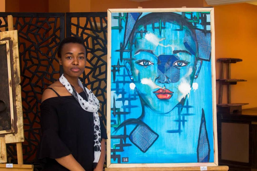 Légende : Mélissa Mujinga pose avec une des oeuvres d'arts.