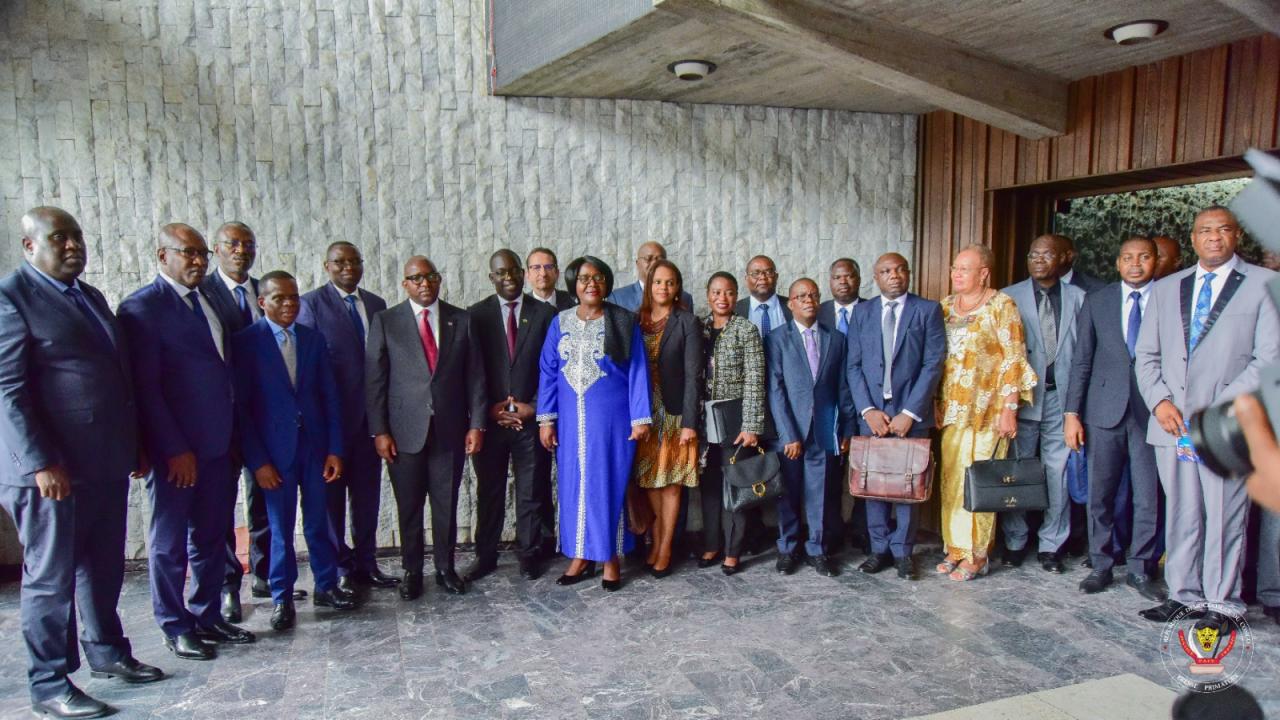 Photo de famille réunissant le Chef du Gouvernement, le ministre Julien Paluku, la délégation zambienne et les parties prenantes au projet de chaîne de valeur des batteries et véhicules électriques