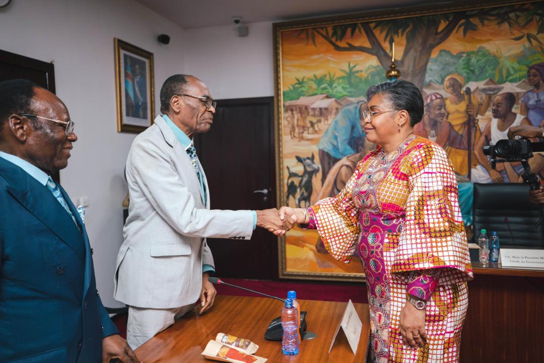 Poignée de main entre la Première Ministre de la RDC, Judith Suminwa, et le chef de la délégation de l'Association des professeurs émérites de la RDC, le prof Baudoin Buassa Bu Tsumbu