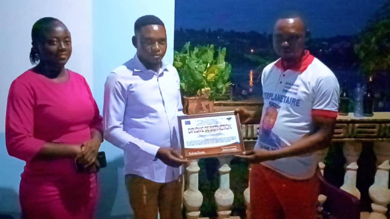 Photo de la remise du diplôme entre le coordonnateur provincial de la JQNA, Bernard Onakana, et le représentant de l’honorable Djosteve.