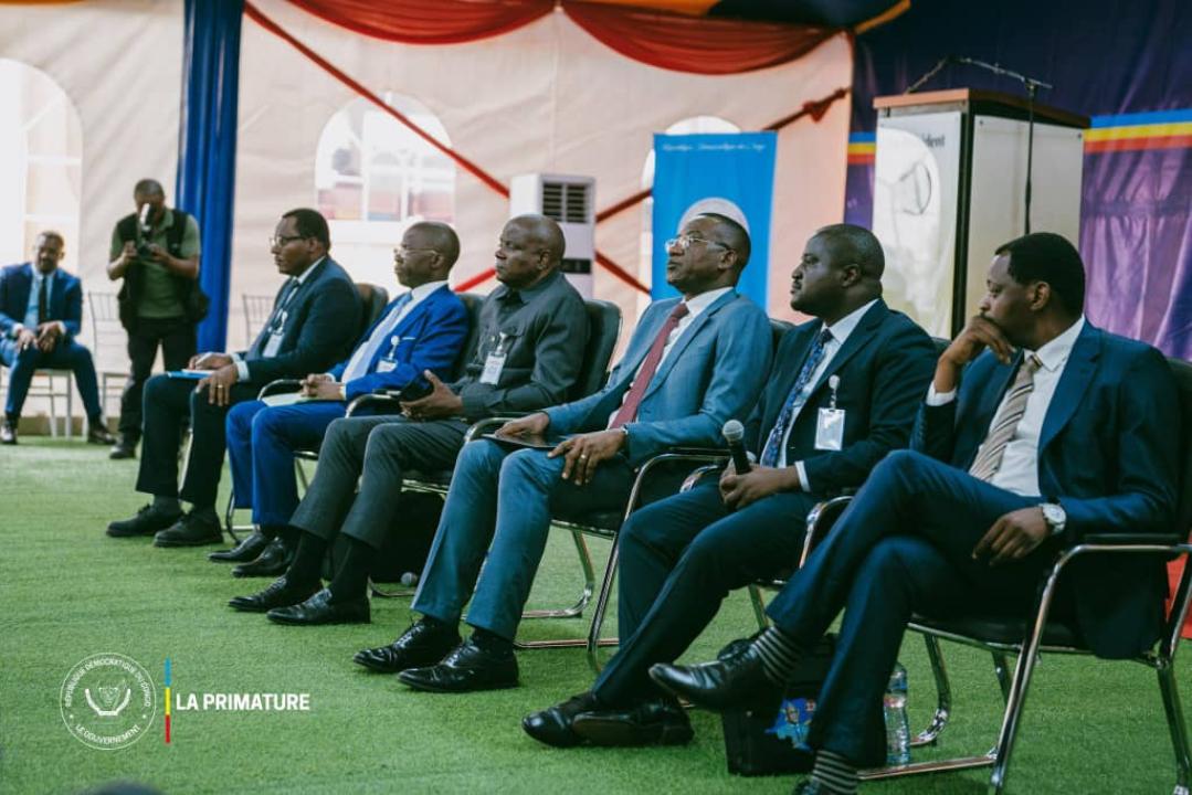 Le ministre Muhindo Nzangi, avec un microphone en mains, assis à la deuxième position, partant de la droite de la photo