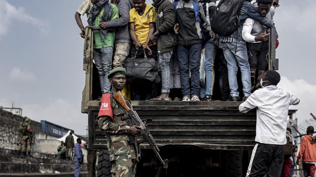 Un combattant du M23 monte la garde pendant que des personnes montent à bord d’un camion lors du recrutement de civils, de policiers, et d’anciens soldats de l’armée congolaise à Goma