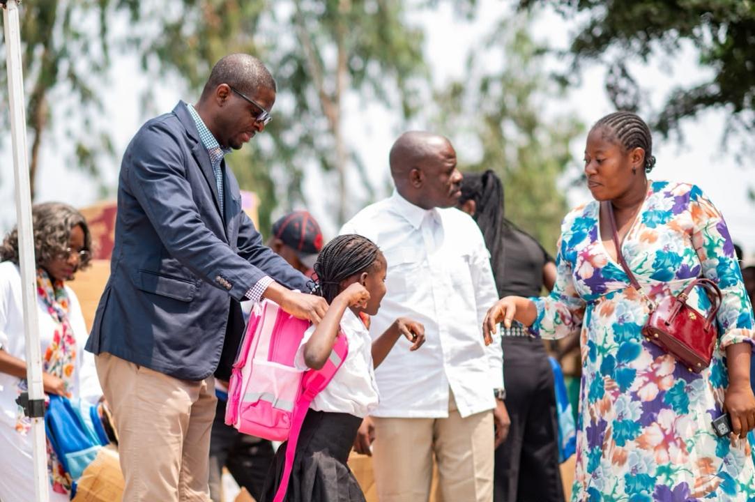 Le député national Éric Tshikuma, élu de la circonscription électorale de la FUNA, aide une écolière à enfiler son cartable lors de la cérémonie de distribution de kits scolaires.